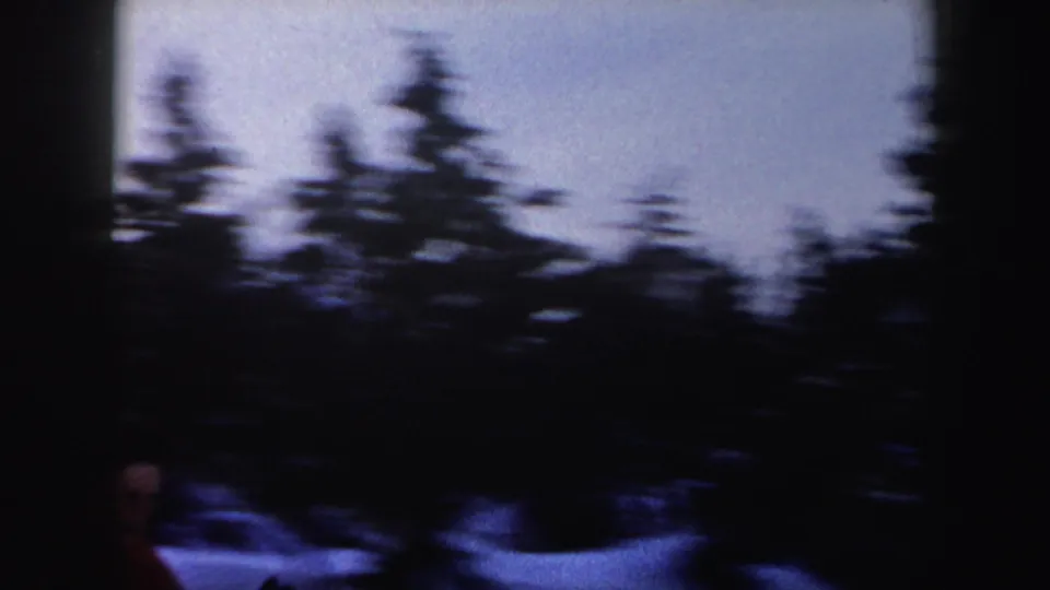 1962 New York 8mm frame with motion blur across dark trees and snow, with part of the skier visible near the lower edge.