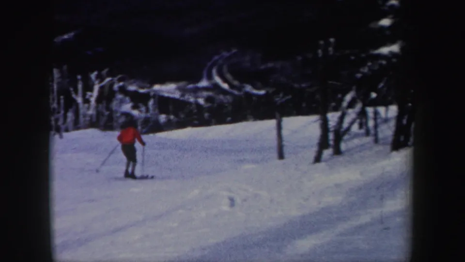 The red-jacketed skier continues downhill on a snowy New York slope, framed by trees in 1962 8mm footage.