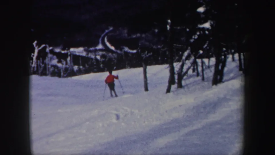A distant skier in a red jacket descends a snowy wooded slope in New York, consistent with the supplied 1962 home-movie metadata.