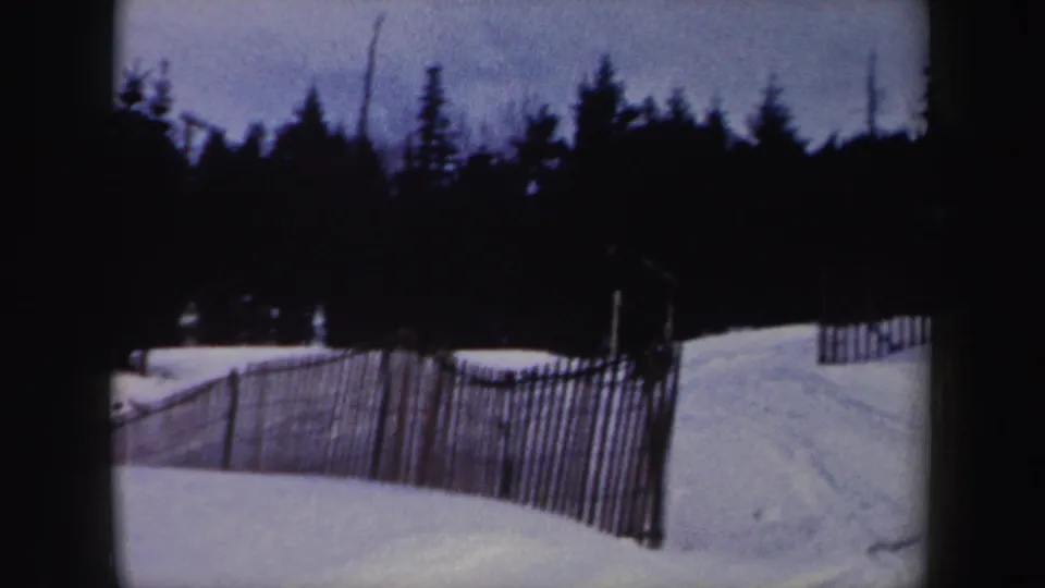 Snow fencing and a quiet snowy slope appear beneath a dark tree line in the 1962 New York ski-area footage.