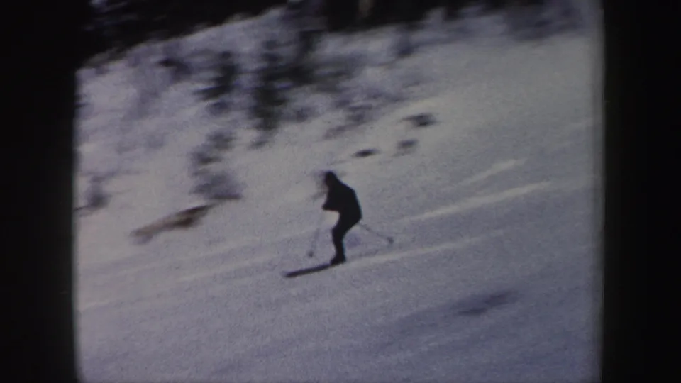 The skier continues across the snow-covered hillside, framed by dark trees in vintage 8mm footage from New York.