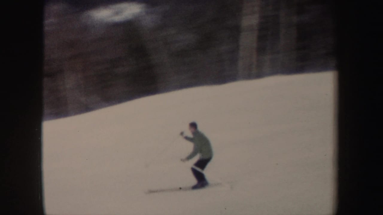 Skier descending a snowy slope with poles, framed by dark film borders.