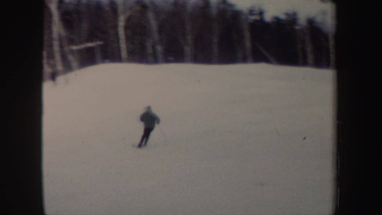 A distant skier crosses a broad snowy slope in New York, with winter trees along the upper edge of the frame.
