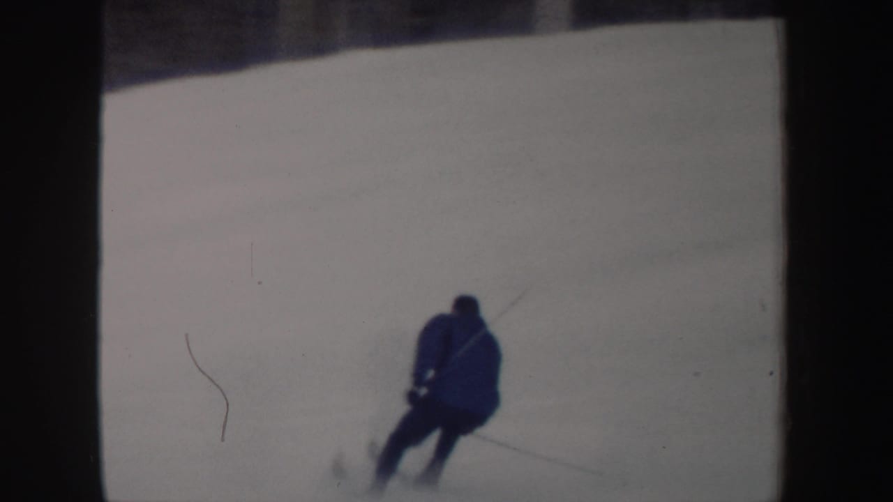 The skier moves away from the camera across the snowy run, holding poles in vintage 8mm footage from New York.