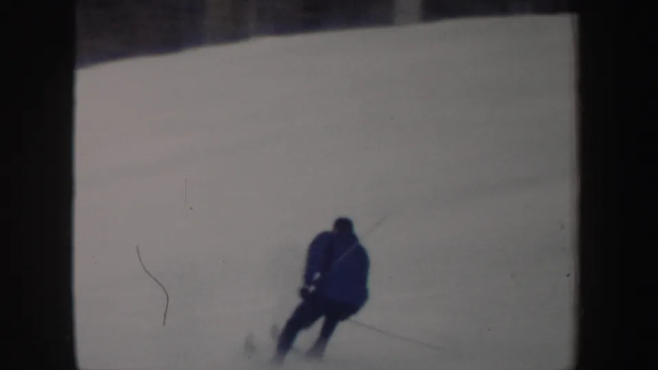 The skier moves away from the camera across the snowy run, holding poles in vintage 8mm footage from New York.