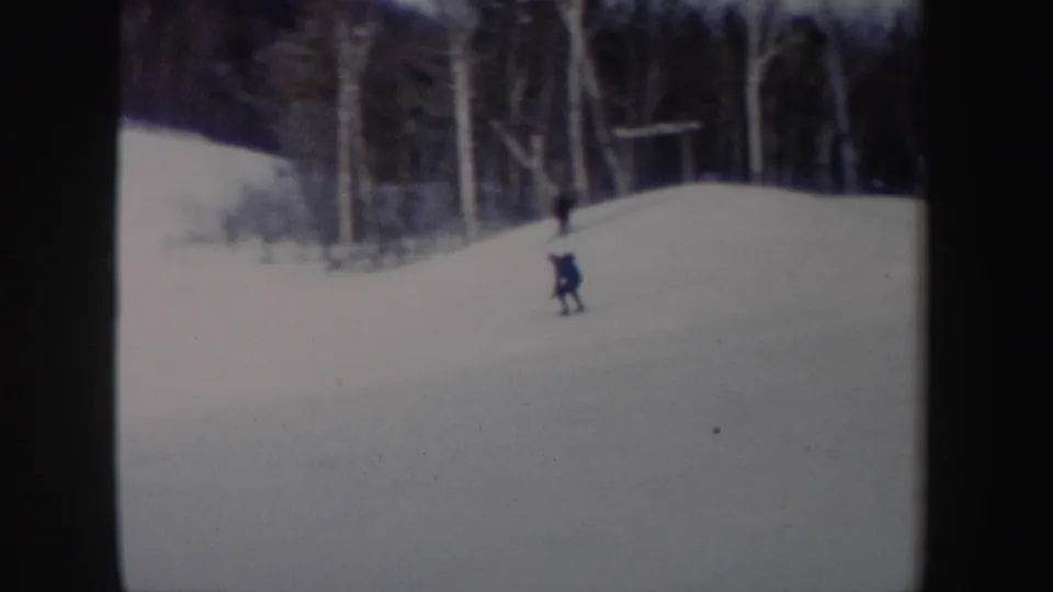 1962 New York 8mm frame showing a distant adult skier descending a snowy wooded slope.