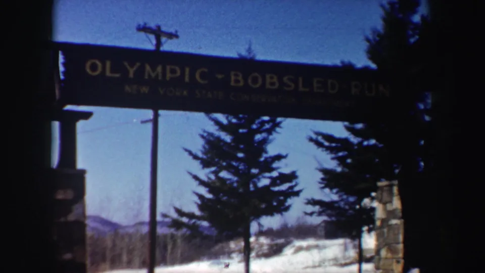 1962 New York home-movie frame showing the Olympic-Bobsled-Run sign and New York State Conservation Department text over snow and trees.