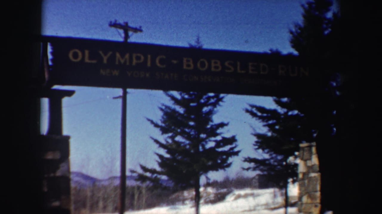 1962 New York 8mm frame showing the Olympic Bobsled Run sign over a stone gateway with snow, evergreens, and distant mountains.