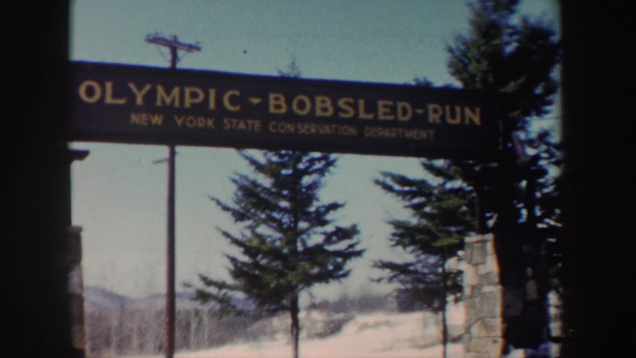 1962 New York 8mm frame showing the Olympic Bobsled Run entrance sign with snow, trees, and distant winter landscape.