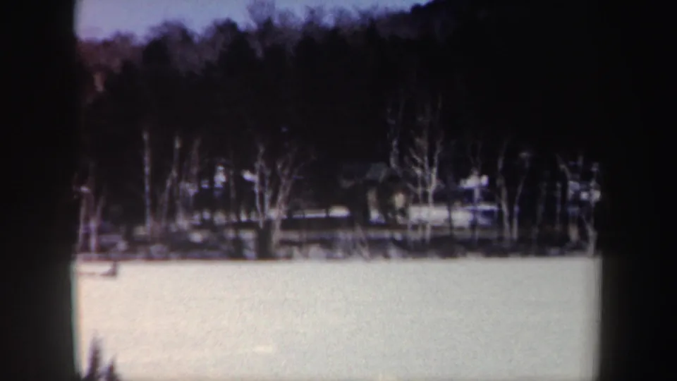 1962 New York 8mm frame with a bright snow-covered lake foreground and a darker line of winter trees along the shore.