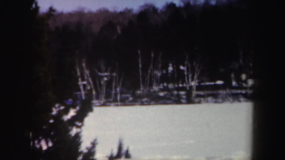 1962 New York winter view with a snow-covered frozen surface, shoreline trees, evergreens, and a small wooden object in the distance.