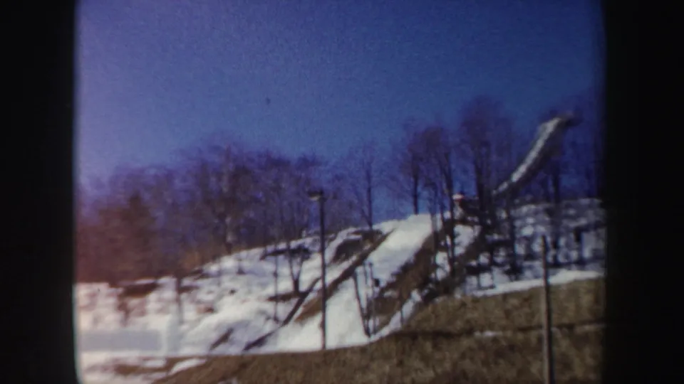 Late frame from the 1962 New York clip with color shift, showing the snowy hillside, bare trees, and curved structure.