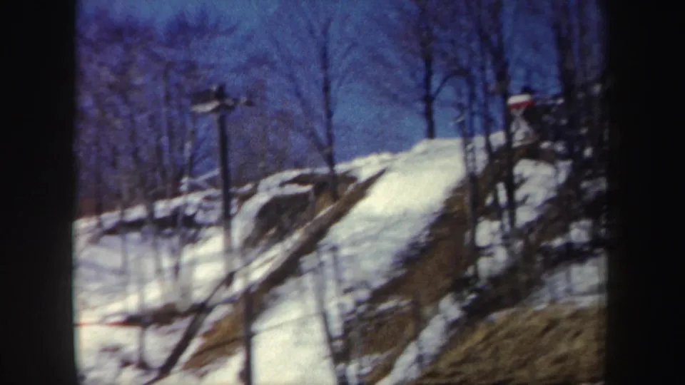 1962 New York winter frame showing snow, leafless trees, posts, and ramp-like structures on a wooded hillside.