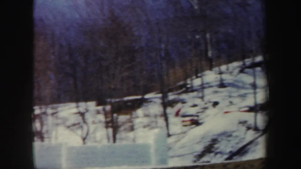 1962 New York 8mm frame of a quiet snow-covered forest slope with leafless trees and dark woods beyond.