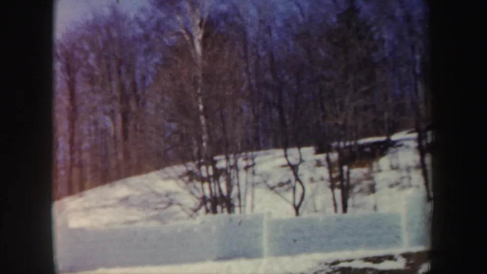 1962 New York winter frame showing a snowbank and open hillside bordered by leafless trees in soft 8mm color.