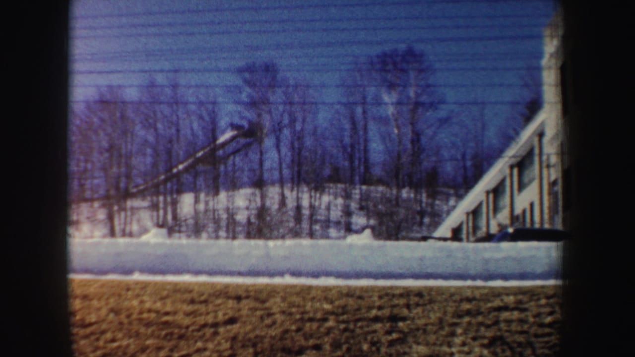 1962 New York 8mm frame showing snow, bare trees, a crane boom, and the edge of a modern building through a dark window frame.