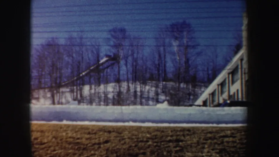 1962 New York frame with a crane over snow-covered ground, leafless trees, and the side of a partly built windowed structure.