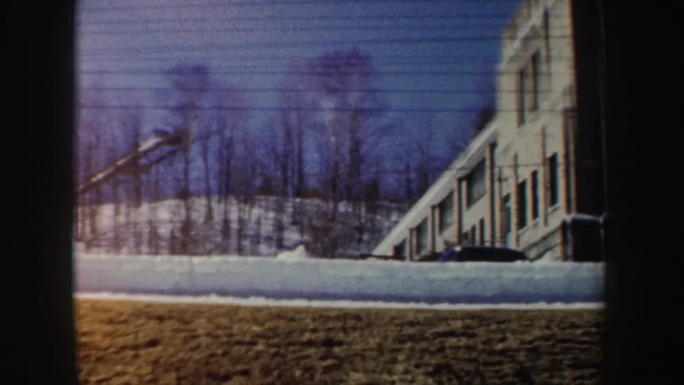1962 New York 8mm frame showing a closer view of the snowy construction area with crane, bare trees, and windowed building facade.