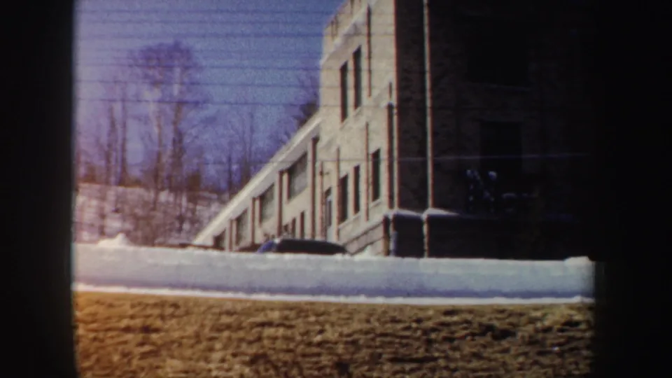1962 New York frame with a partly built windowed structure beside snowbanks and bare trees, with the crane partly visible at left.