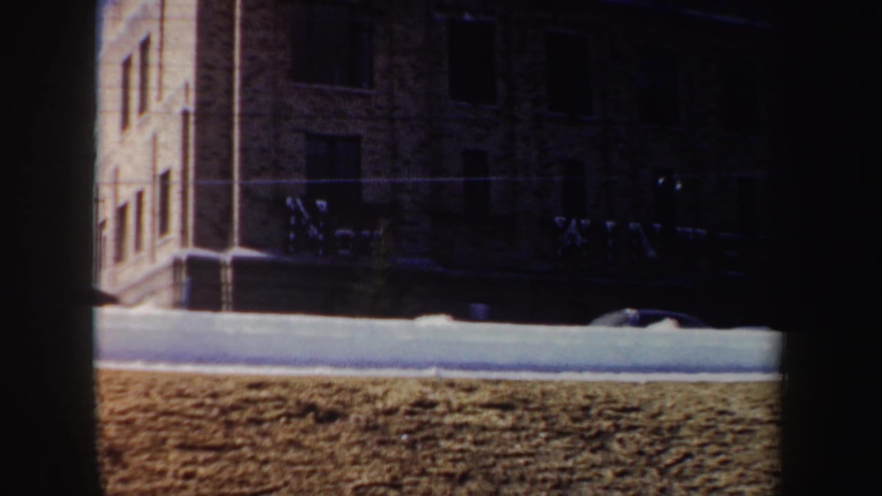 Front of a brick building with snowbank, lawn, windows, and dark vertical film edge.