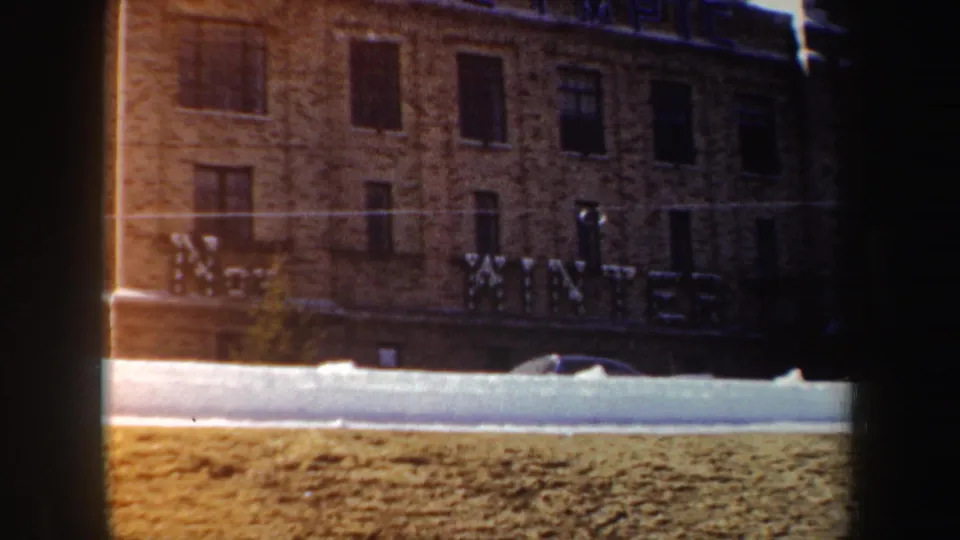 1962 New York 8mm frame showing a brick building with large WINTER lettering, snow on the ground, and a car near the curb.