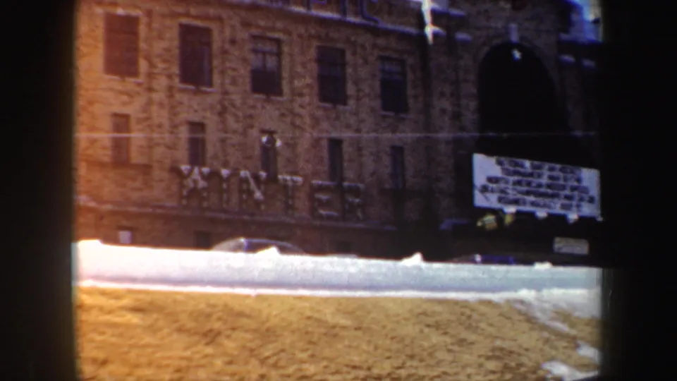 1962 New York 8mm frame showing a brick building, large WINTER lettering, an arched entry, snowbank, and a bright signboard.