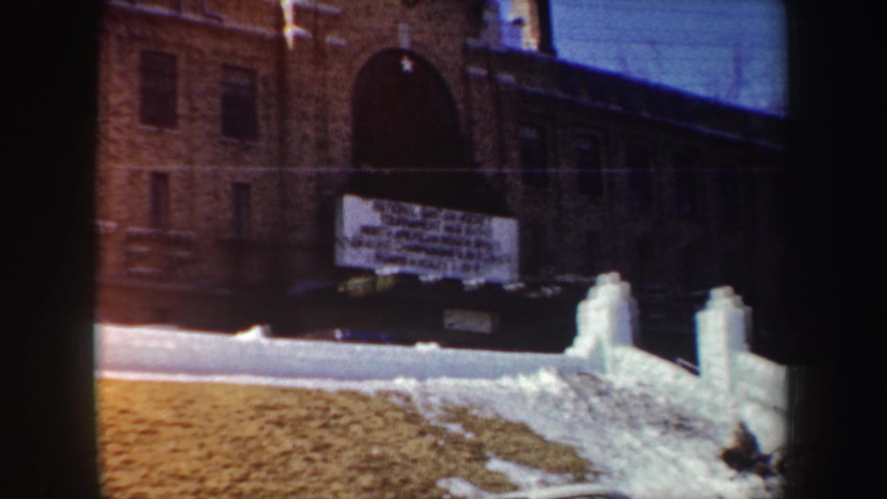 Brick building exterior with snowbanks and a hanging sign near an arched doorway.