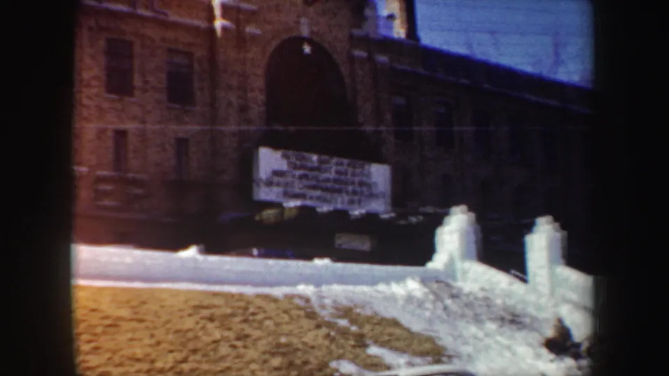 1962 New York winter exterior with a brick building, arched doorway, snow-covered ground, and a prominent hanging sign.