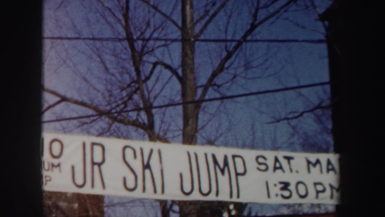 1962 New York 8mm frame showing a white JR SKI JUMP event banner partially cropped against bare trees, power lines, and winter sky.