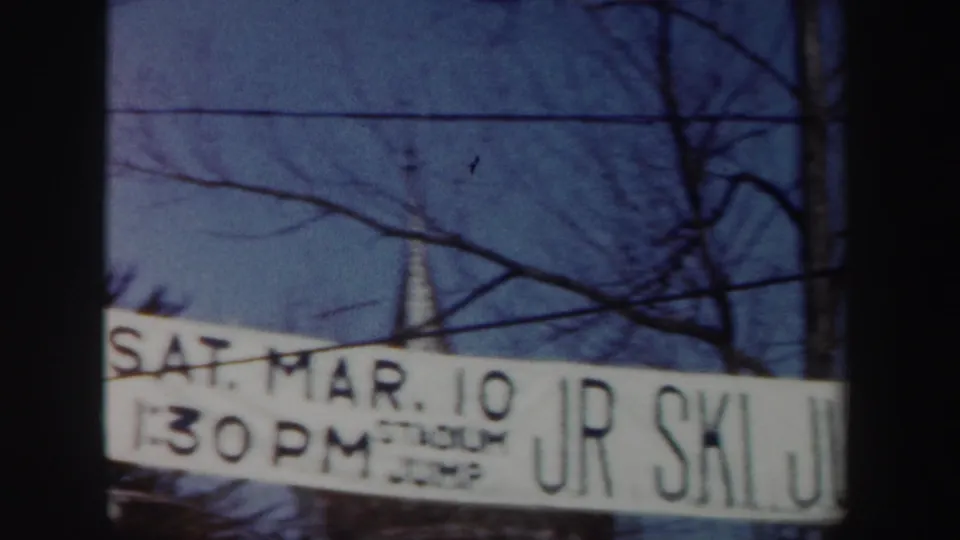 1962 New York 8mm frame with the ski-jump banner showing SAT. MAR. 10, 1:30 PM, and partial JR SKI JUMP lettering above snow-covered surroundings.