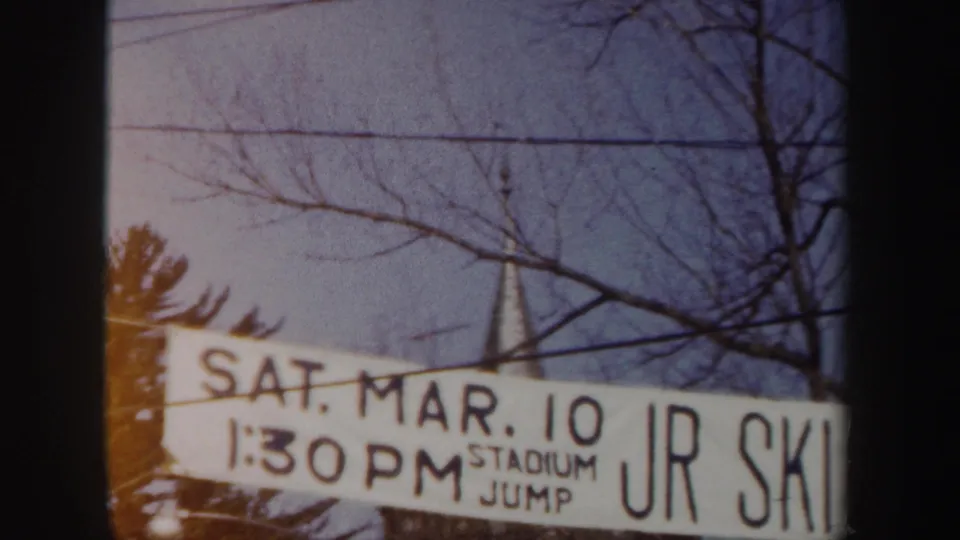 1962 New York 8mm frame showing a closer section of the ski-jump banner with SAT. MAR. 10, 1:30 PM, STADIUM JUMP, and partial JR SKI text.