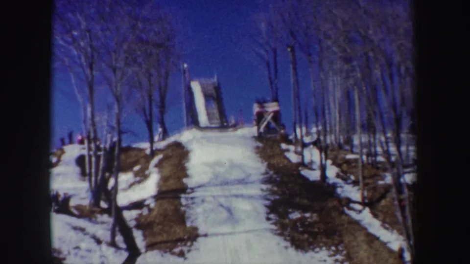 1962 New York 8mm frame with a closer uphill view of the snow-covered slope and ski jump structure among bare trees.