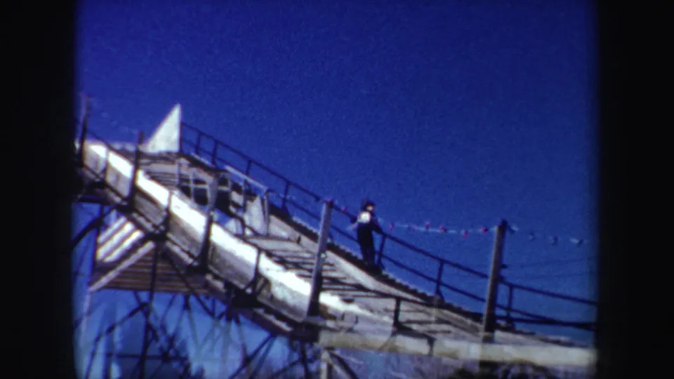 Home-movie frame of a worker on a steep planked structure with metal railings, shot in New York in 1962.