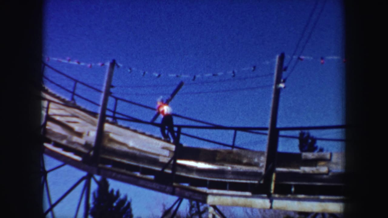 Skier carrying skis up a steep wooden ramp under a blue sky.