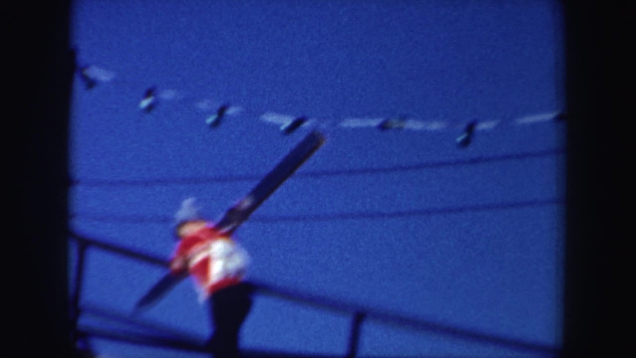 A soft, close view shows the skier carrying skis near the ramp railings, with wires or string lights against a deep blue sky.
