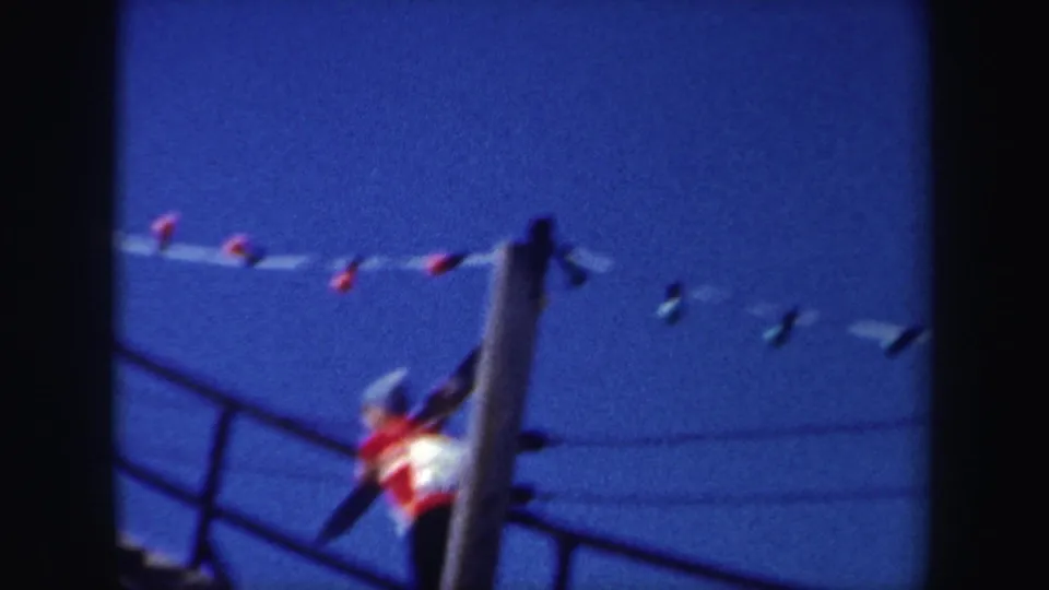 Near the end of the 1962 New York clip, the skier continues upward past a pole, with railings and overhead lights visible against the sky.