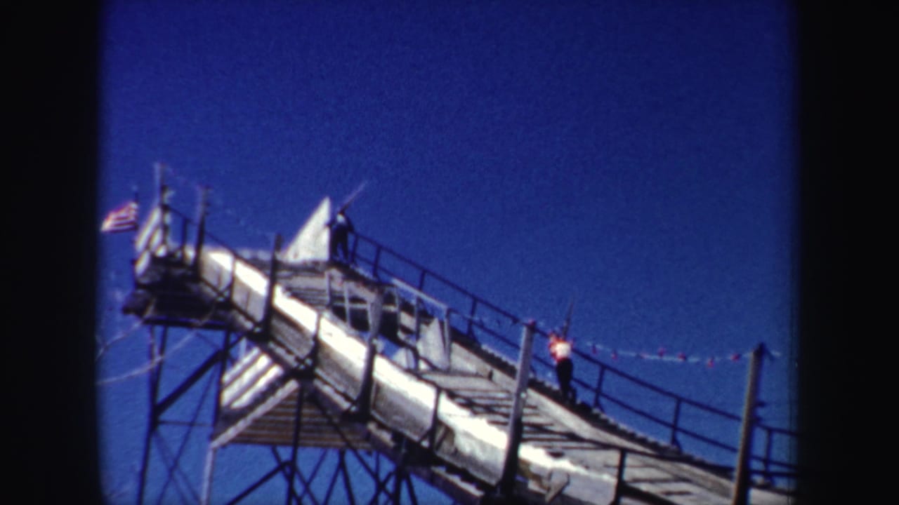 Wooden ski-jump ramp against a deep blue sky with an American flag visible near the top.