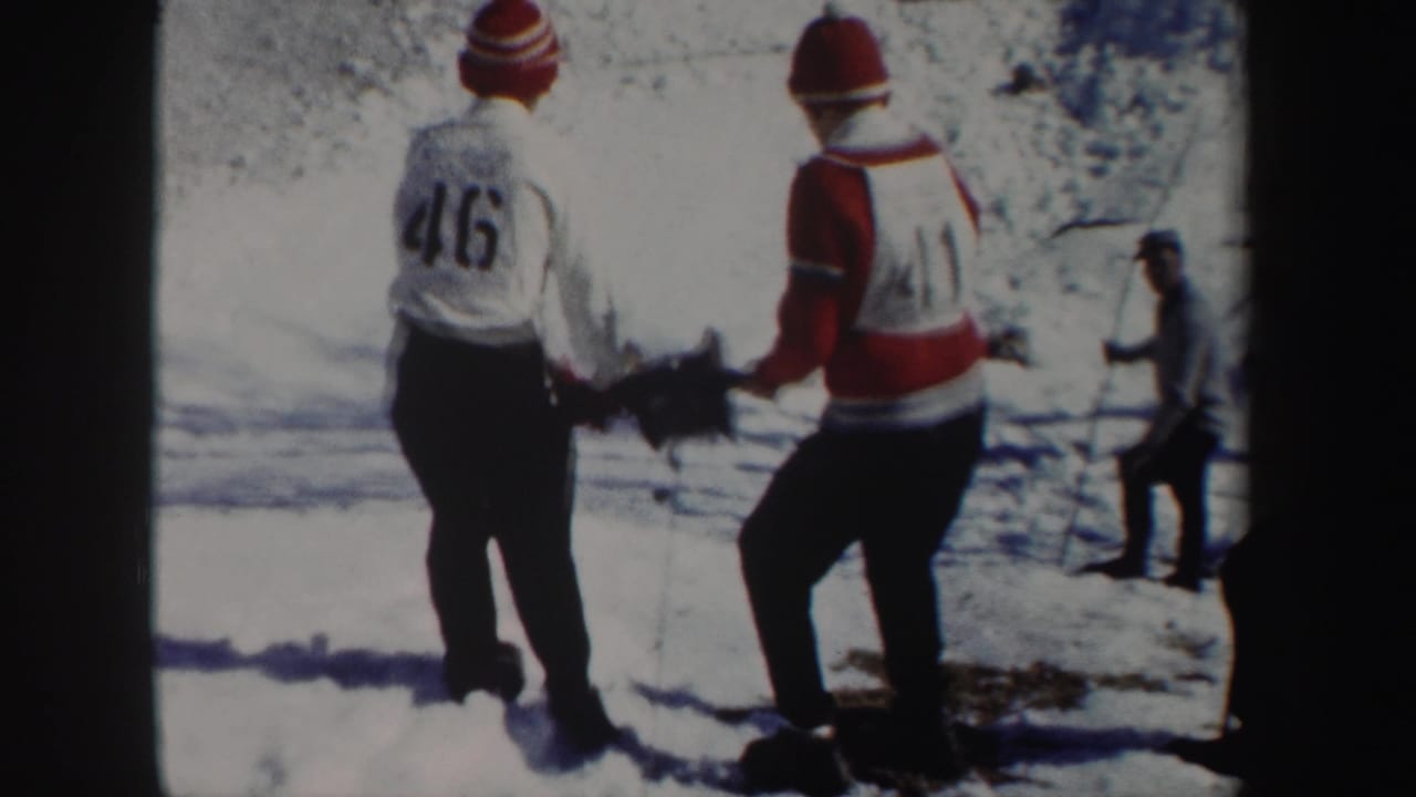 1962 New York 8mm frame showing two young men in red winter hats working with a reel or line tool on a snowy slope.