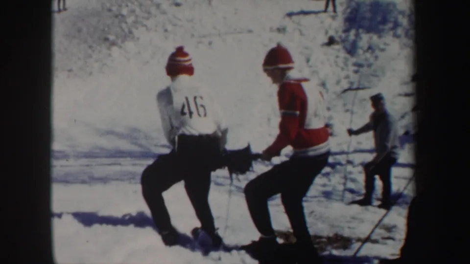 1962 New York home-movie frame with two young men in winter gear handling a reel or line across bright snow.