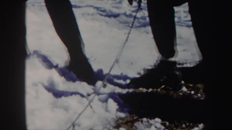 Close 1962 New York 8mm frame showing lower legs, snow tracks, and a cord or reel at the edge of the action.