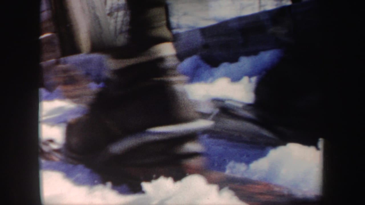 Close view of ski boots or lower legs moving over snow near a dark frame edge.