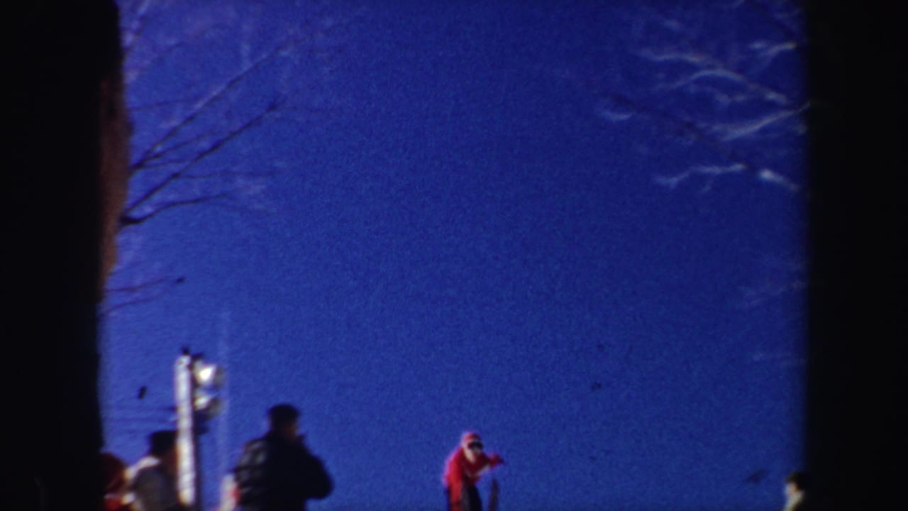 Skier in a red sweater stands near a snowy slope under a deep blue sky.
