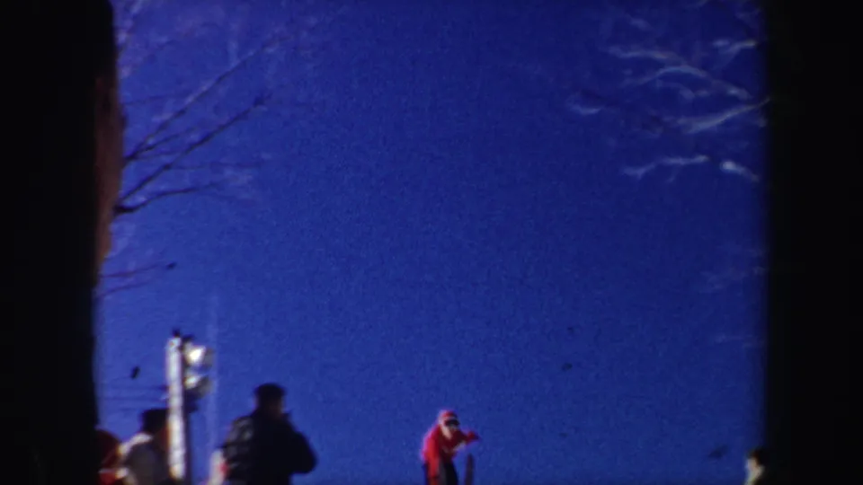 1962 New York 8mm frame showing a red-sweatered skier near snow and onlookers under a saturated blue sky.