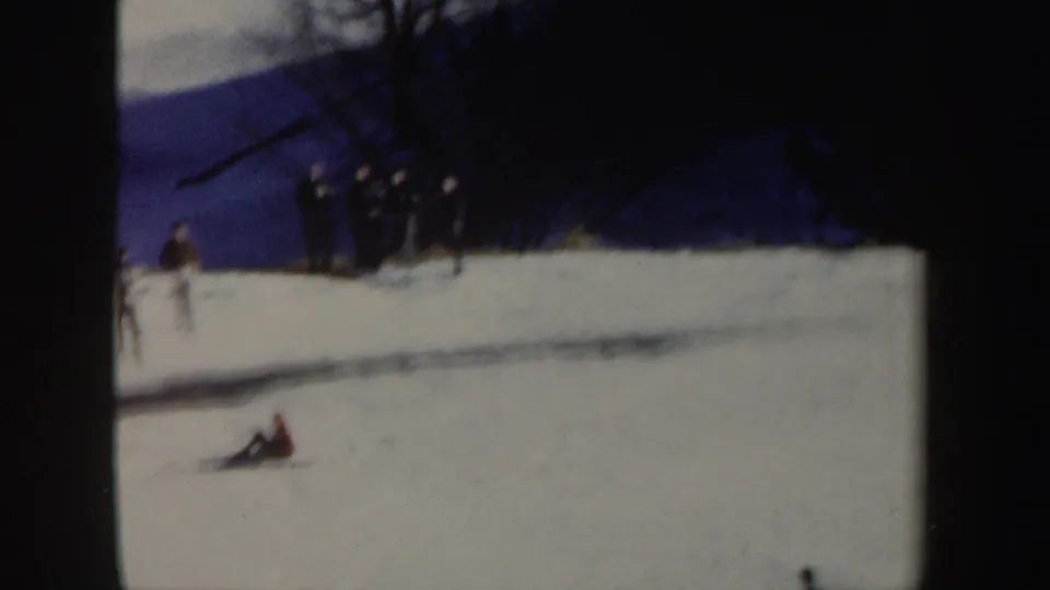 1962 New York 8mm frame showing the skier down on a snowy slope after the jump, with spectators in the background.