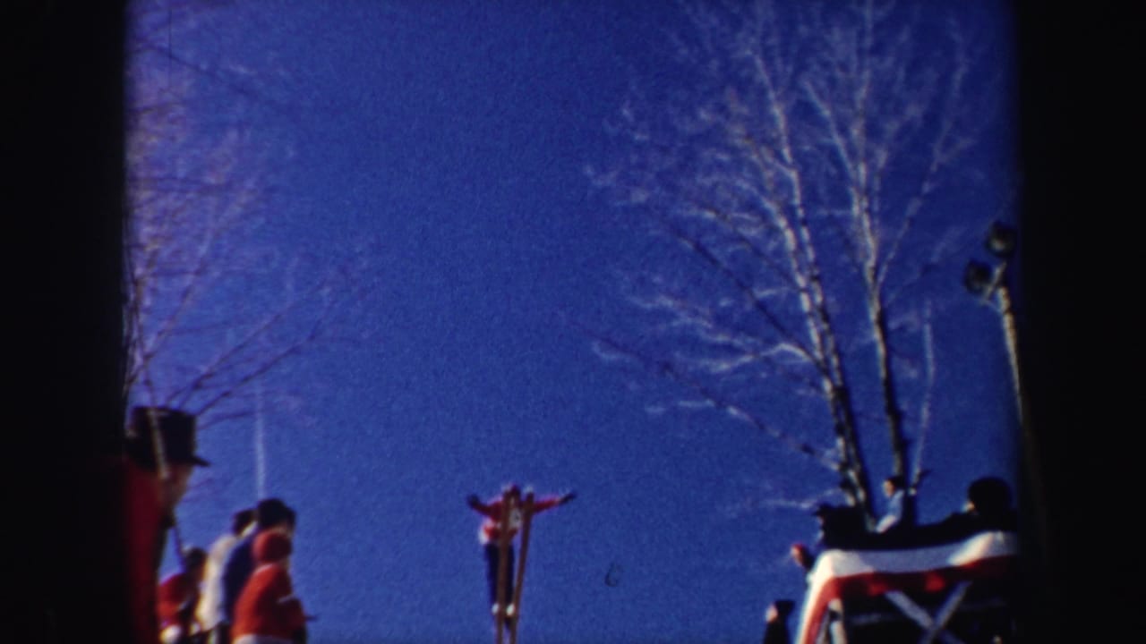 1962 New York 8mm frame of a skier launching from a snowy jump while a small crowd watches under a deep blue sky.