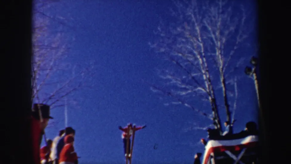 1962 New York 8mm frame of a skier launching from a snowy jump while a small crowd watches under a deep blue sky.