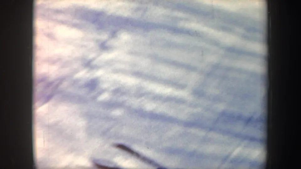Soft 8mm frame of snow texture and tracks during the skiing sequence, with motion blur obscuring the subject.