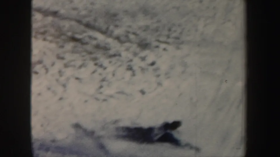 1962 New York 8mm frame of a skier down in the snow after a fall, seen from a distance on a textured slope.