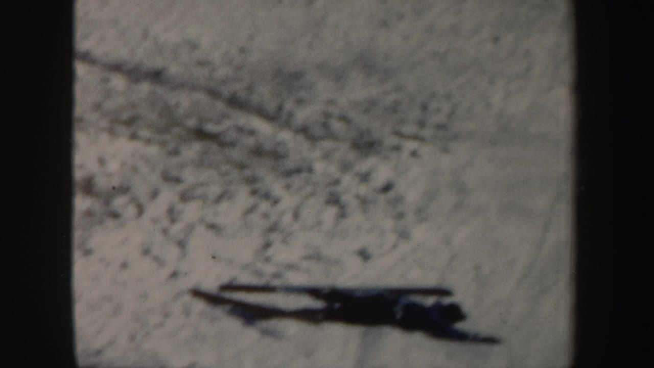 Dark skier shape crossing a snowy slope near the edge of an 8mm frame.