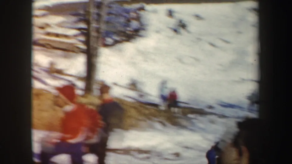1962 New York ski-area view with bundled people gathered near snow, trees, and rail-like fencing in soft 8mm color.